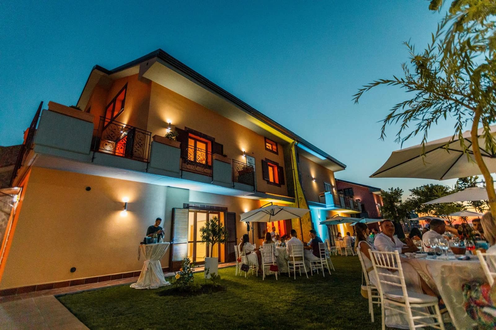 Fațada Vilei Oro la lăsarea serii, cu invitați la mese în grădină
