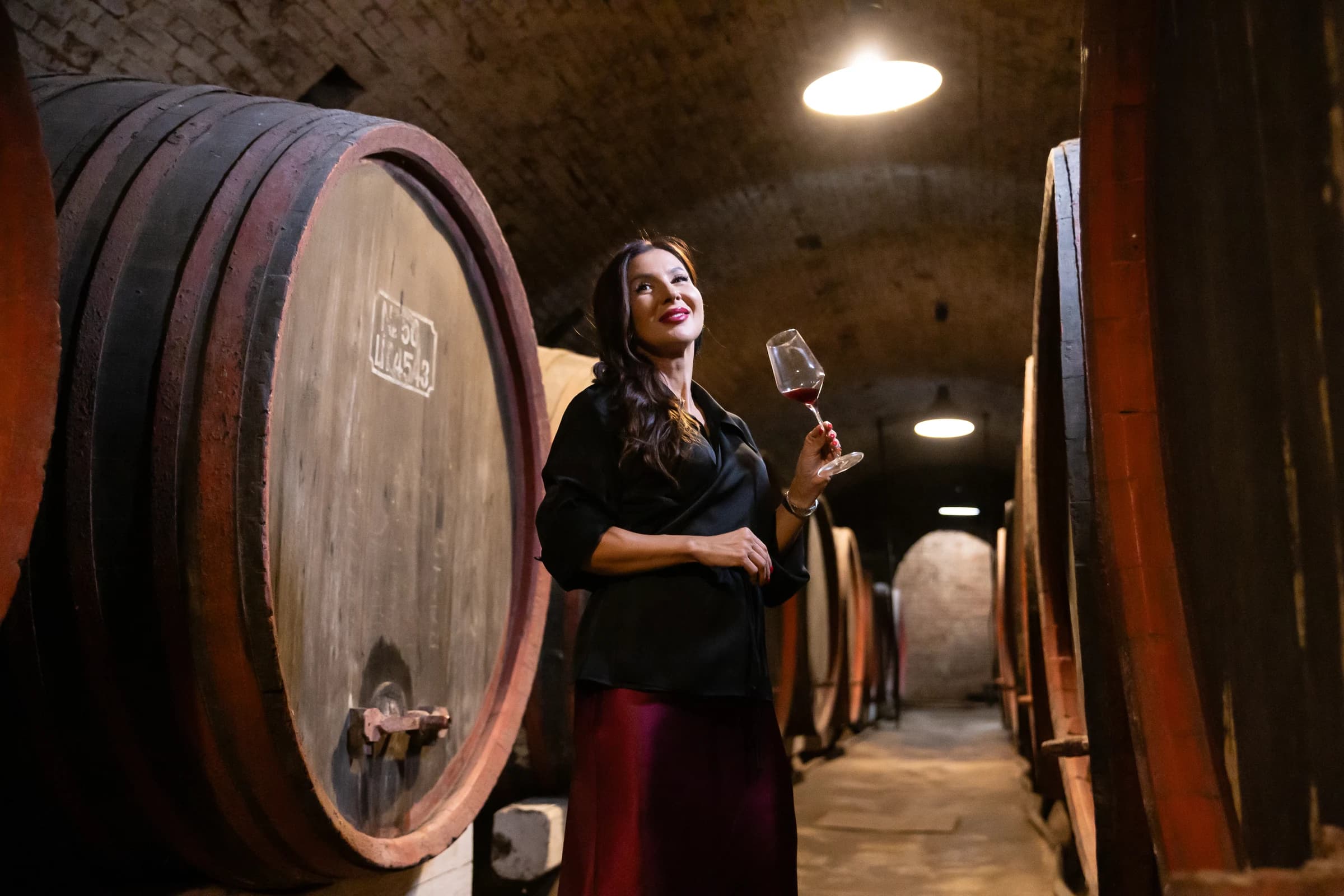 Roxana cu un pahar de vin, între butoaie mari de lemn